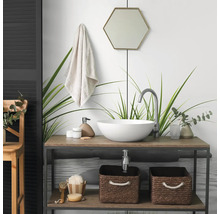 Moderne badkamer met een ronde opzetwastafel op een houten wastafelmeubel, een hoge kraan, een zeshoekige spiegel en gevlochten opbergmanden.