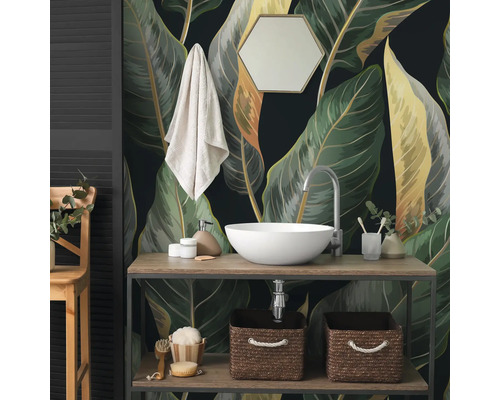 Fotobehang met grote botanische bladeren in de badkamer achter een houten wastafelmeubel met witte opzetkom en accessoires.