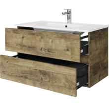 Modern badmeubel met twee open lades in eikenlook, inclusief witte keramische wastafel en verchroomde kraan.