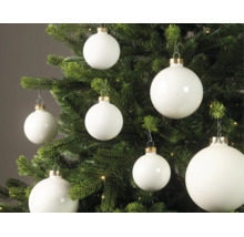 Witte kerstballen in matte en glanzende uitvoering hangend in een groene kerstboom met lichtjes.