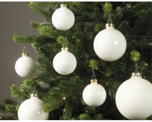 Witte kerstballen in matte en glanzende uitvoering hangend in een groene kerstboom met lichtjes.
