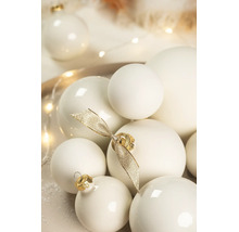 Diverse crèmewitte kerstballen met een matte en glanzende afwerking, versierd met een gouden strik.