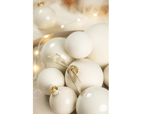 Diverse crèmewitte kerstballen met een matte en glanzende afwerking, versierd met een gouden strik.
