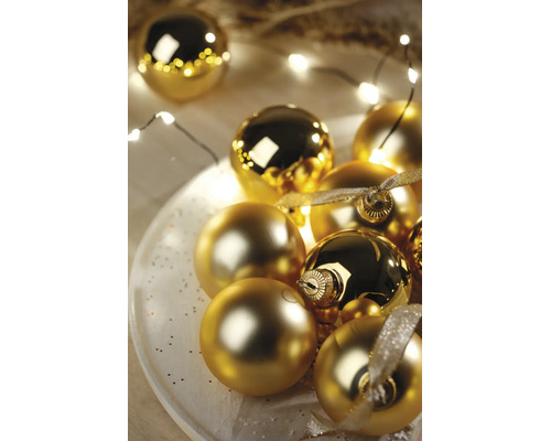 Feestelijke opstelling van gouden kerstballen in glanzende en matte uitvoering op een wit bord met LED-lichtsnoer en decoratielint.