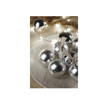 Zilveren kerstballen met glanzende en matte afwerking op een bord, versierd met strikken en kerstverlichting.