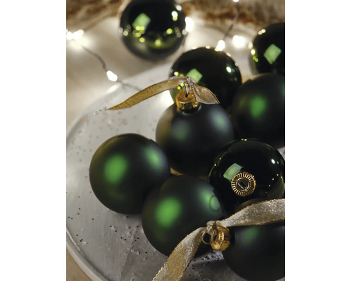 Donkergroene kerstballen in matte en glanzende uitvoering met gouden linten en feestelijke verlichting.