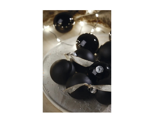 Zwarte kerstballen in matte en glanzende uitvoering op een bord met zilveren linten en feestelijke verlichting.