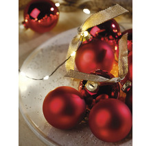 Kerstdecoratie met rode kerstballen in mat en glanzend, een gouden decoratielint en een lichtsnoer op een bord.