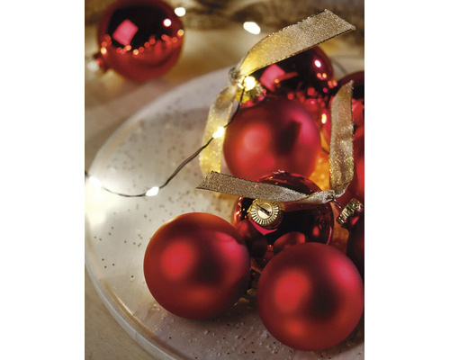 Kerstdecoratie met rode kerstballen in mat en glanzend, een gouden decoratielint en een lichtsnoer op een bord.
