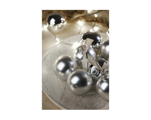 Zilveren kerstballen met glanzende en matte afwerking op een bord, versierd met strikken en kerstverlichting.