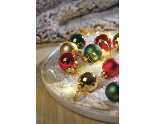 Feestelijke opstelling van kerstballen in rood, groen en goud op een dienblad met kunstsneeuw en LED-lichtsnoer.