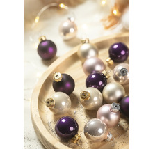 Glazen kerstballen in paars en crème op een ronde houten schaal.