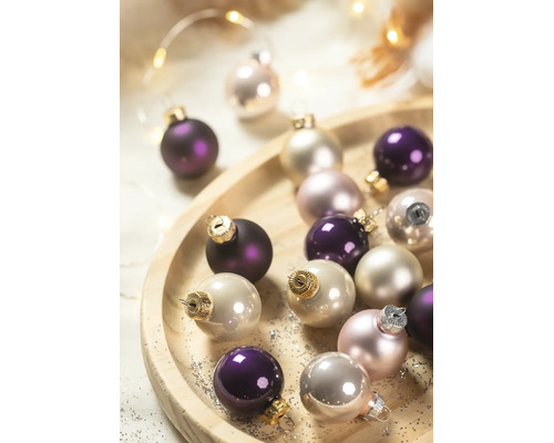 Glazen kerstballen in paars en crème op een ronde houten schaal.