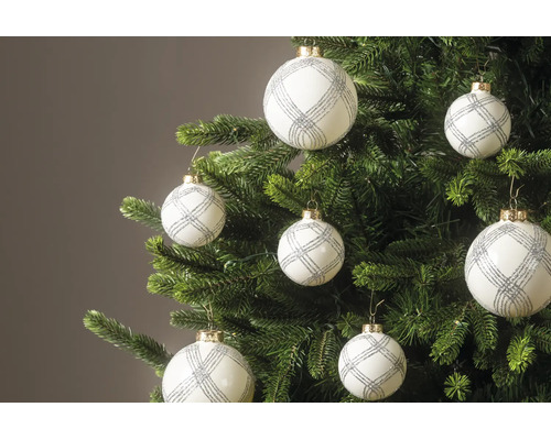 Witte kerstballen met zilveren glitterpatroon hangen aan de takken van een groene kerstboom.