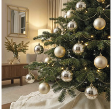 Versierde kerstboom met zilveren en champagnekleurige ballen, verlichting en gouden slingers in een lichte woonkamer.