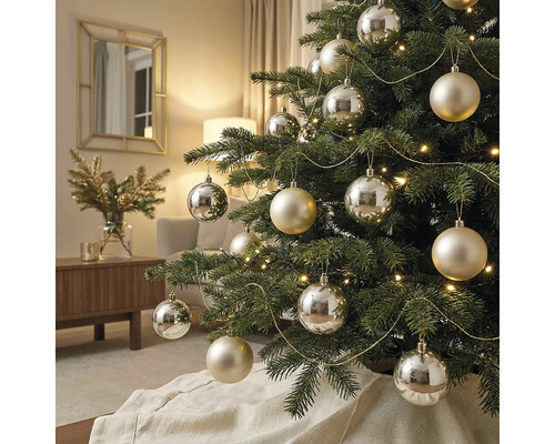 Versierde kerstboom met zilveren en champagnekleurige ballen, verlichting en gouden slingers in een lichte woonkamer.