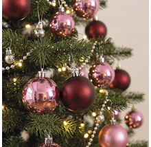 Kerstboom versierd met glanzende roze en matte donkerrode kerstballen, een parelsnoer en een warmwitte lichtslinger.