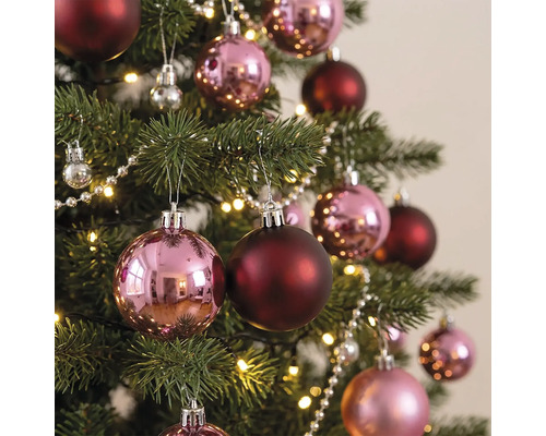 Kerstboom versierd met glanzende roze en matte donkerrode kerstballen, een parelsnoer en een warmwitte lichtslinger.