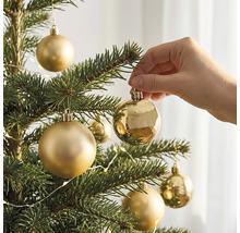 Een hand hangt een glanzende gouden kerstbal in een kerstboom met matte en glanzende kerstballen.