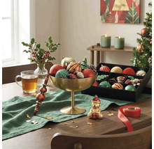 Feestelijk versierde houten tafel met gouden schaal vol kerstversiering, een zwarte opbergdoos, groene loper en een glas thee.