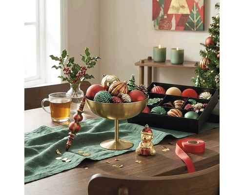 Feestelijk versierde houten tafel met gouden schaal vol kerstversiering, een zwarte opbergdoos, groene loper en een glas thee.