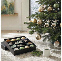 Kerstboom versierd met kerstballen, uilen- en hertfiguren naast een opbergdoos met kerstversiering op een tapijt.