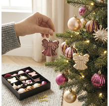 Een hand hangt een engelvormige versiering in een verlichte kerstboom met kerstballen en sterren naast een doos met meer kerstdecoratie.