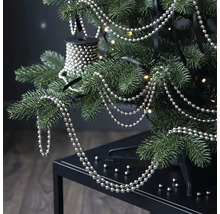 Zilveren parelsnoer aan de takken van een kerstboom met warmwitte lichtjes.