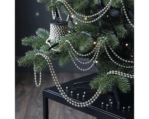Zilveren parelsnoer aan de takken van een kerstboom met warmwitte lichtjes.