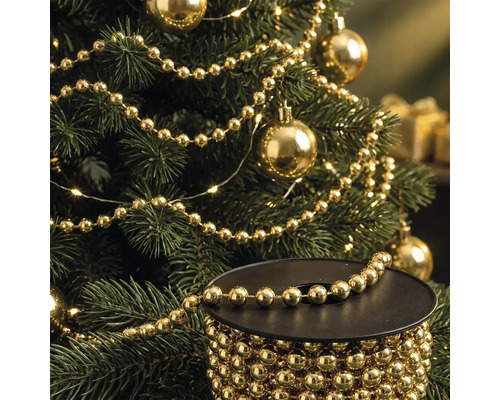 Kerstboom versierd met gouden parelslinger en kerstballen, met op de voorgrond een spoel met de gouden parelslinger.