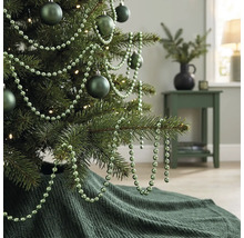 Gedecoreerde kerstboom met matte kerstballen, kralenslinger en een gebreide kerstboomrok in een woonkamer.