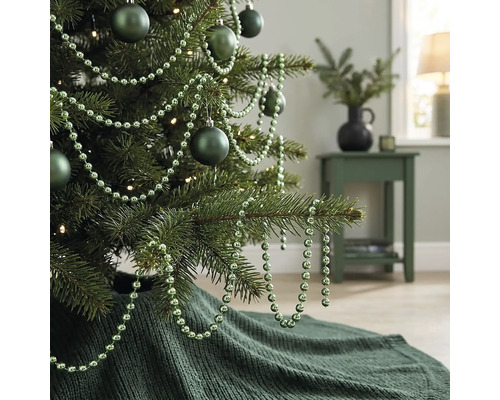 Gedecoreerde kerstboom met matte kerstballen, kralenslinger en een gebreide kerstboomrok in een woonkamer.