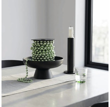 Groene kralenslinger op een zwarte decoratieve schaal, met een zwarte kandelaar en een glas water op een lichte tafel.