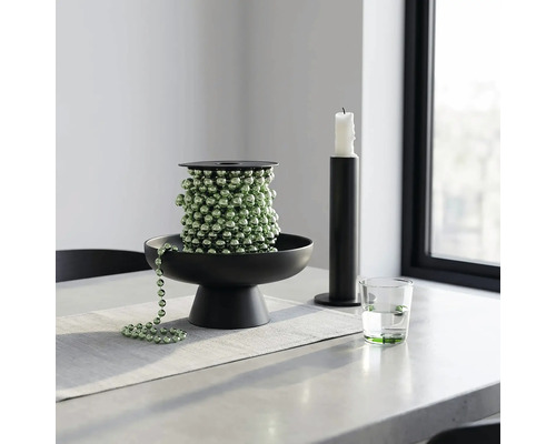 Groene kralenslinger op een zwarte decoratieve schaal, met een zwarte kandelaar en een glas water op een lichte tafel.