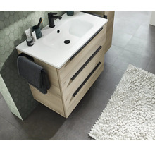 Modern wastafelmeubel in lichte houtlook met drie laden, zwarte handgrepen en een witte wastafel met een zwarte kraan.