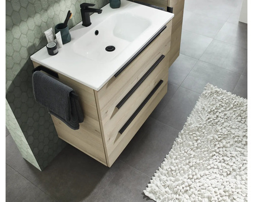 Modern wastafelmeubel in lichte houtlook met drie laden, zwarte handgrepen en een witte wastafel met een zwarte kraan.
