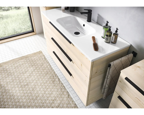 Modern wastafelmeubel van licht hout met drie lades, zwarte handgrepen, witte keramische wastafel en zwarte kraan in een lichte badkamer.