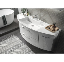 Moderne, lichte badkamer met gebogen wastafelmeubel, twee laden en kraan. In de achtergrond een vrijstaand ligbad en wandtegels.