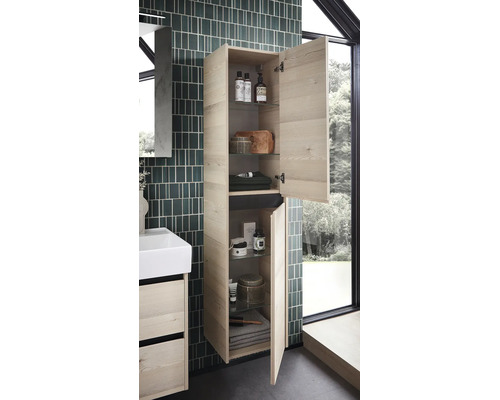 Wandhangende hoge badkamerkast in lichte houtlook met twee geopende deuren, glazen legplanken en badkameraccessoires naast een wastafelmeubel.