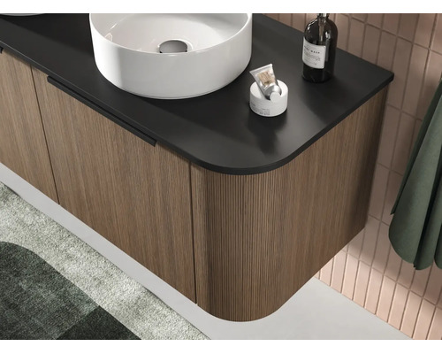 Moderne hangende wastafelonderkast met verticaal gegroefd front in houtlook, zwart blad en witte opzetwastafel.