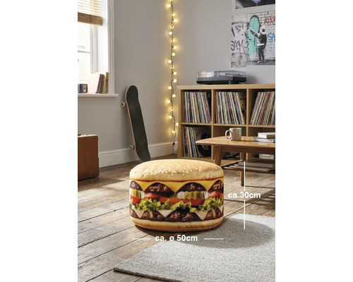 Een ronde poef met hamburgerontwerp, circa 30 centimeter hoog en circa 50 centimeter in diameter, in een lichte kamer met een houten vloer.