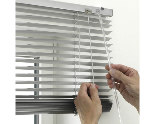 Detailopname van een hand die een zilveren aluminium jaloezie bedient met een transparante tuimelstaaf en trekkoord.