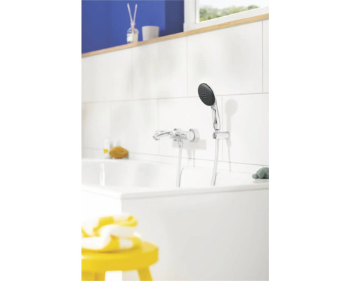 Verchroomde badkraan met handdouche op een witte tegelwand boven een wit ligbad in een lichte badkamer.