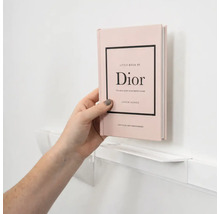 Een hand plaatst het boek Little Book of Dior op een smalle witte wandplank.