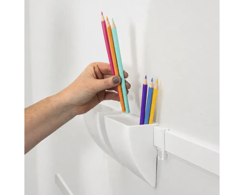Een hand plaatst kleurpotloden in een witte wandorganizer voor het opbergen van schrijfgerei.