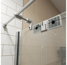 Detail van een douchecabine met een metalen stabilisatiestang, een glazen wand en witte wandtegels.