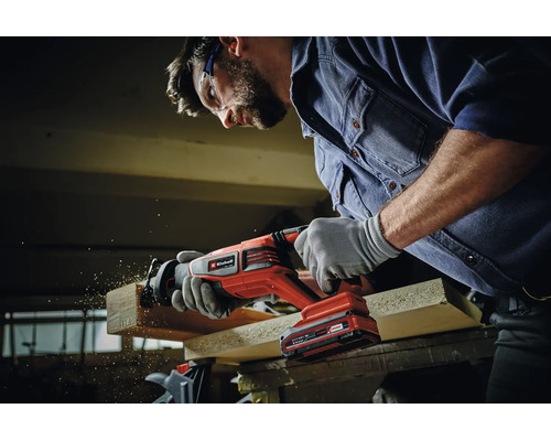 Vakman met veiligheidsbril gebruikt een Einhell accu reciprozaag om een houten plank door te zagen in de werkplaats.