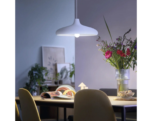 Moderne hanglamp boven een eettafel in een lichte, sfeervolle eetkamer met een boeket bloemen en decoratie.