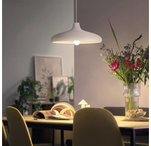 Moderne hanglamp boven een eettafel met een boeket bloemen en decoratie op de achtergrond in een lichte woonkamer.