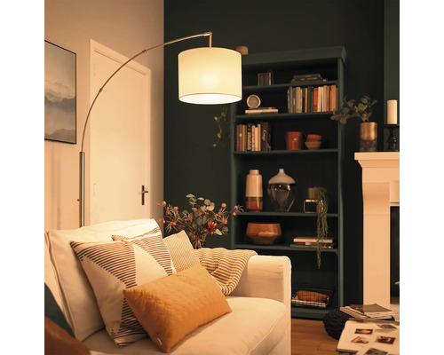 Moderne booglamp met stoffen kap naast een bank in een gezellig ingerichte woonkamer met een donkere kast en een haard.